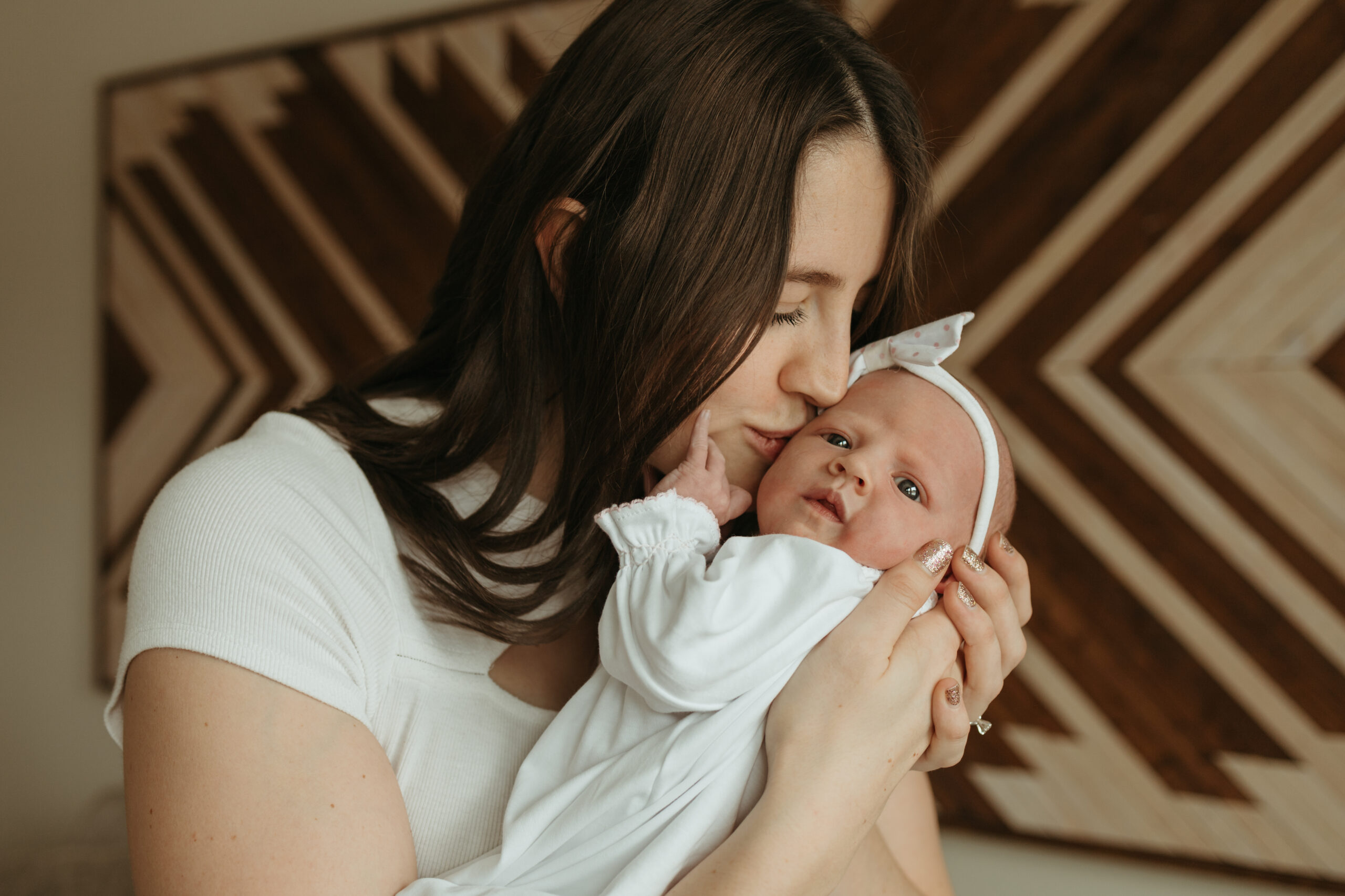 Mom-kissing-newborn-baby-wearing-white-bow-during-in-home-newborn-session-in-Longmont-Colorado-with-Alexis-Adkins-Photography