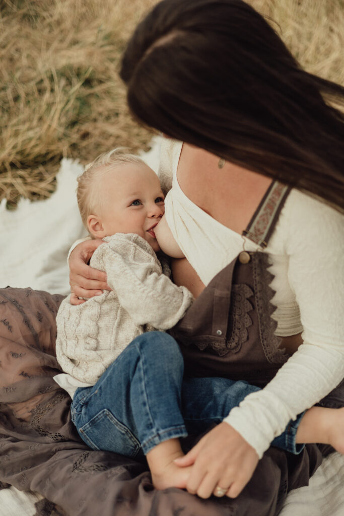 Toddler-Breastfeeding-While-looking-up-and-smiling-at-mom-alexis-adkins-photography-lifestyle-in-home-newborn-and-maternity-photographer