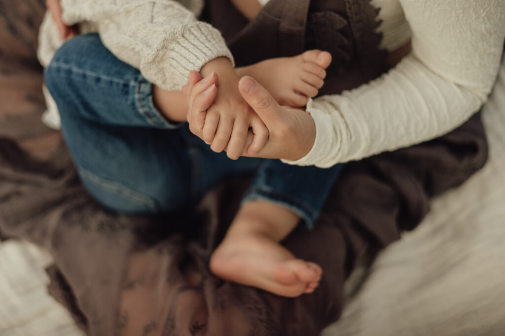 mom-and-toddler-holding-hands-while-breastfeeding-in-longmont-colorado-during-breastfeeding-session-with-alexis-adkins-photography