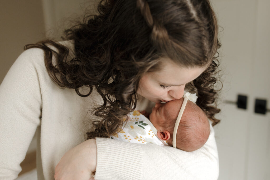 Longmont Mom holding newborn baby girl kissing newborns forehead during in home newborn session with alexis adkins photo