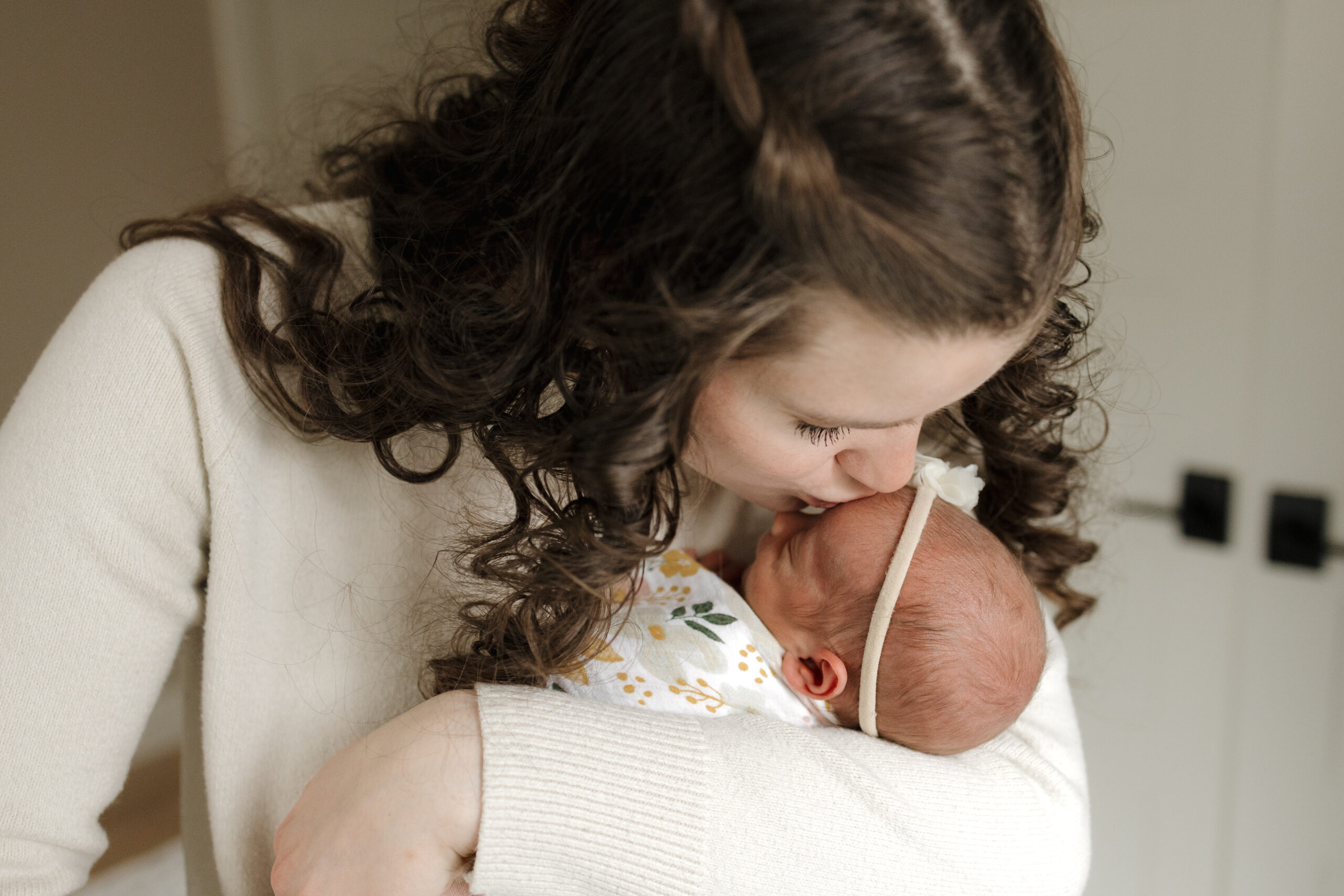 Longmont Mom holding newborn baby girl kissing newborns forehead during in home newborn session with alexis adkins photo