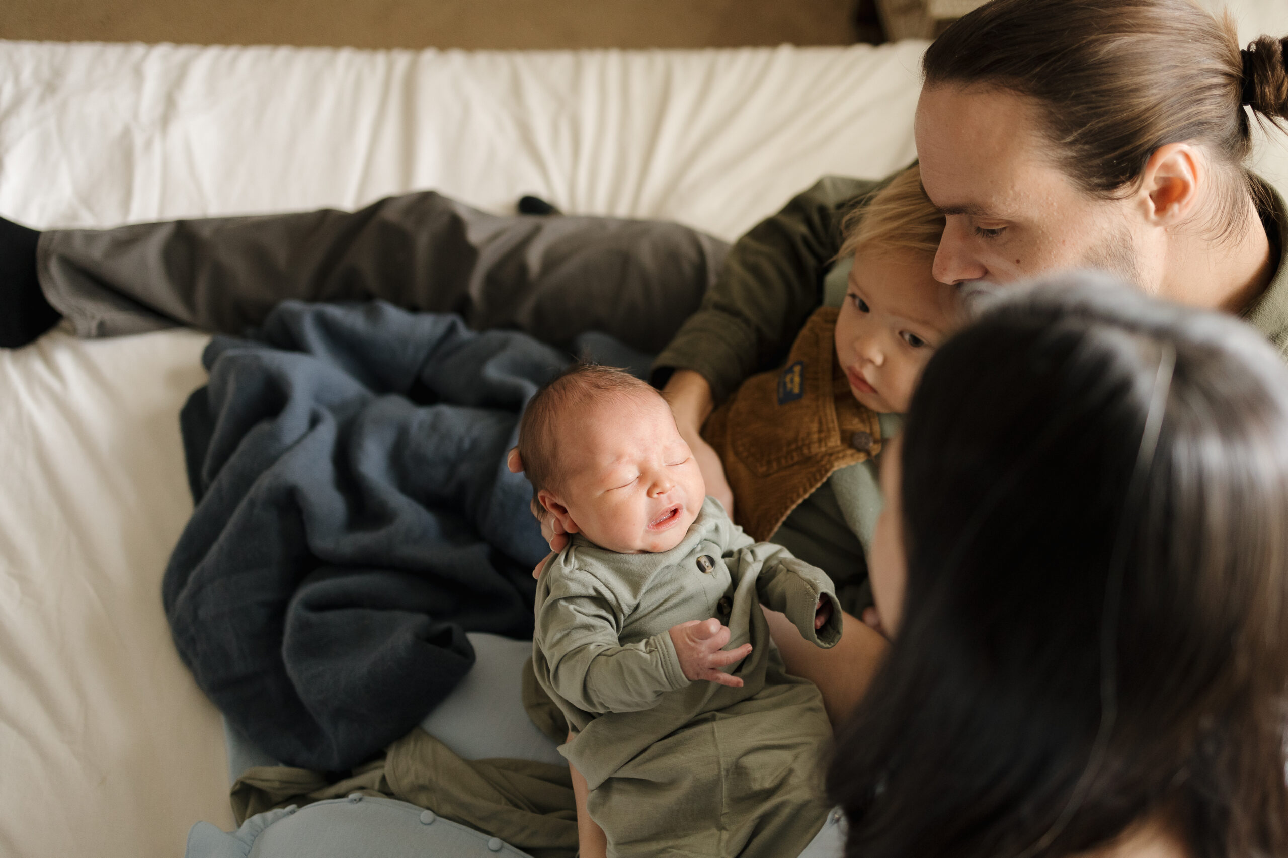 Family sitting on bed loving on new baby during newborn session in longmont colorado with alexis adkins photography
